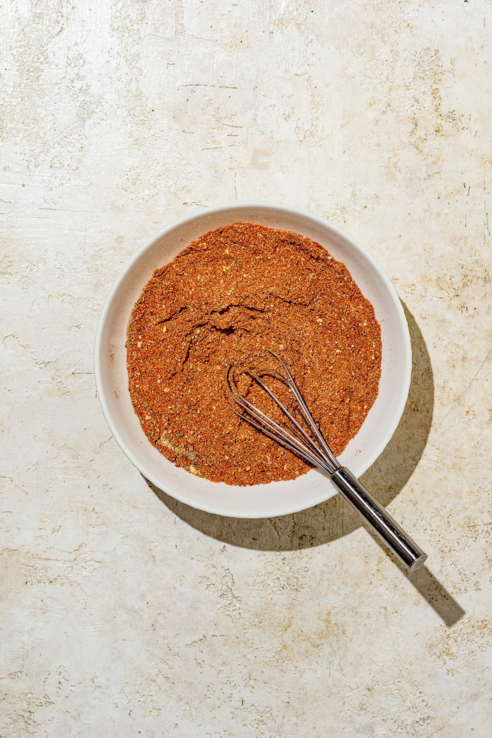 A large white bowl with a whisk mixing Red Robin seasoning. The bowl is on a tan counter.