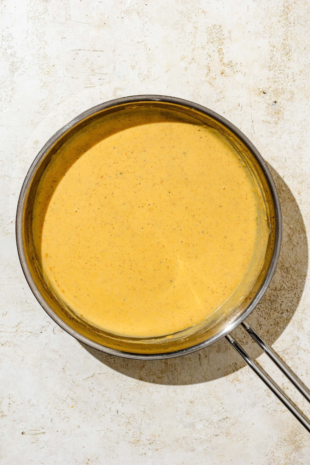A skillet with cooked Buffalo mac and cheese sauce. The skillet is on a tan counter.
