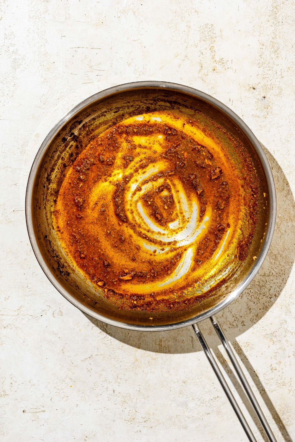 A skillet a roux made with oil, seasonings, and flour. The skillet is on a tan counter.