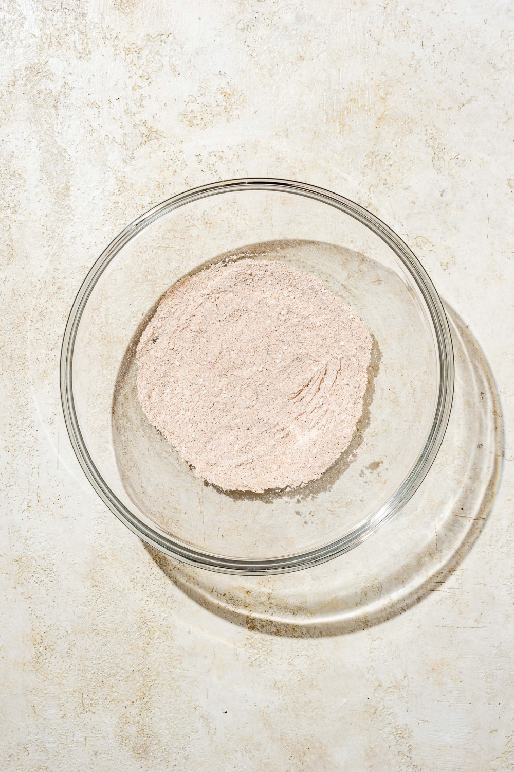 A glass bowl with a seasonings mixture including garlic powder, salt, pepper, and paprika. The bowl is on a tan counter.