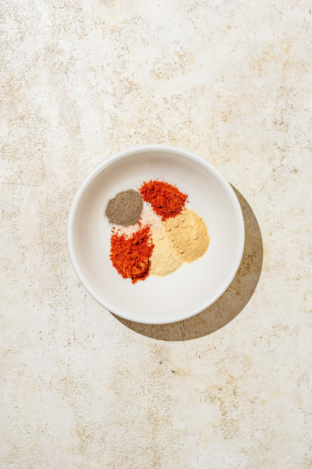 A white bowl with a variety of seasonings for hot honey chicken. The bowl is on a tan counter.