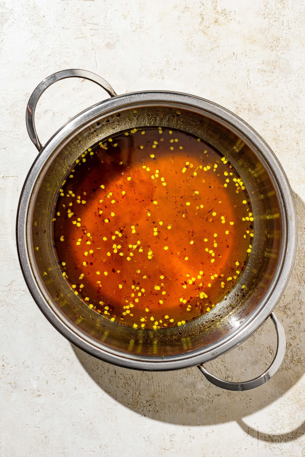 A stock pot with cooked candied jalapeños sauce. The pot is on a tan counter.