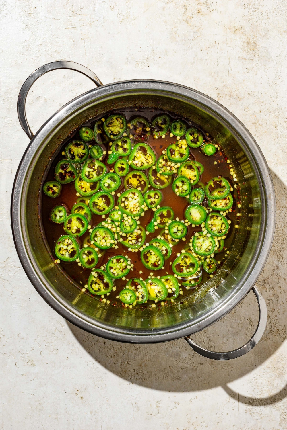 A stock pot with sliced jalapeños cooking in candied jalapeño sauce. The pot is on a tan counter.