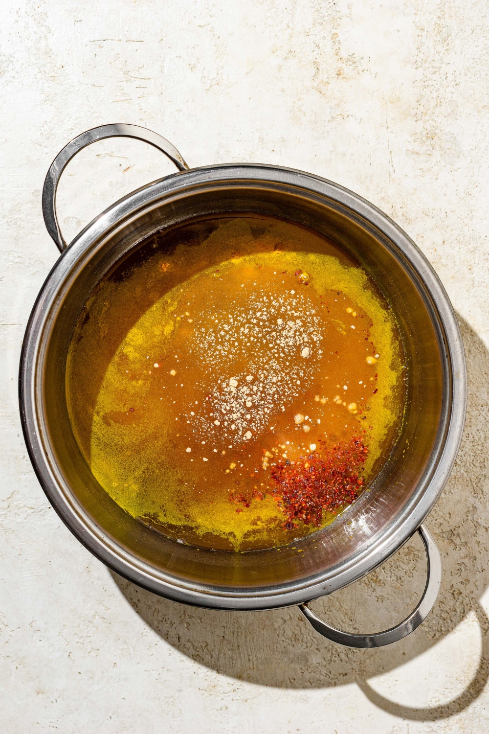 A stock pot with ingredients to make candied jalapeños sauce including apple cider vinegar, white sugar, brown sugar, and spices. The pot is on a tan counter.