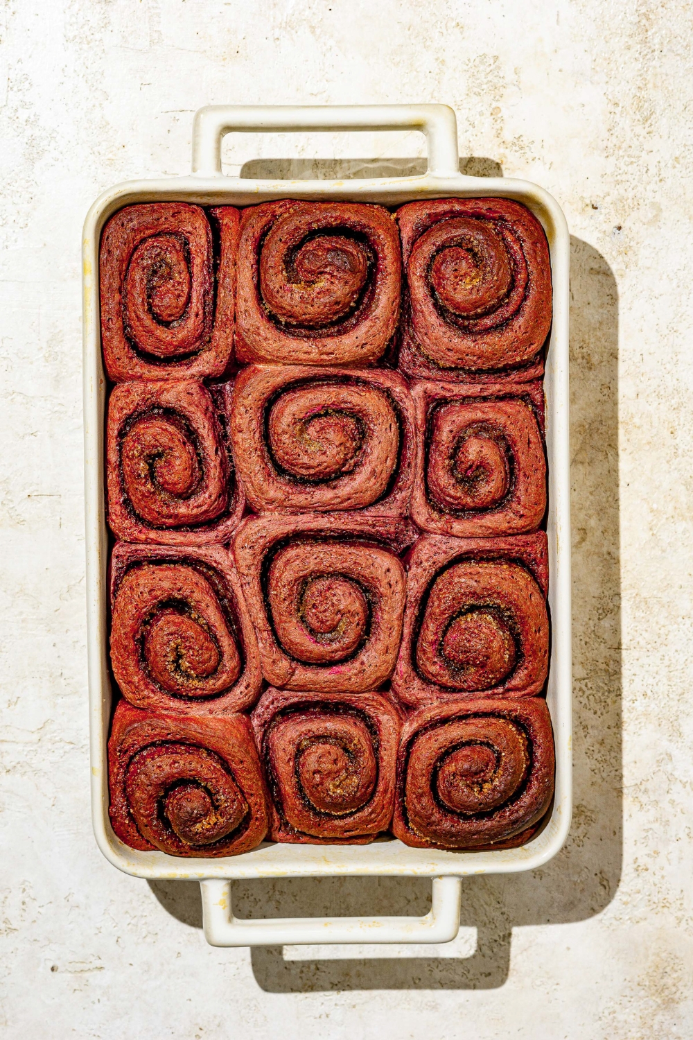 A baking dish with baked red velvet cinnamon rolls. The dish is on a tan counter.