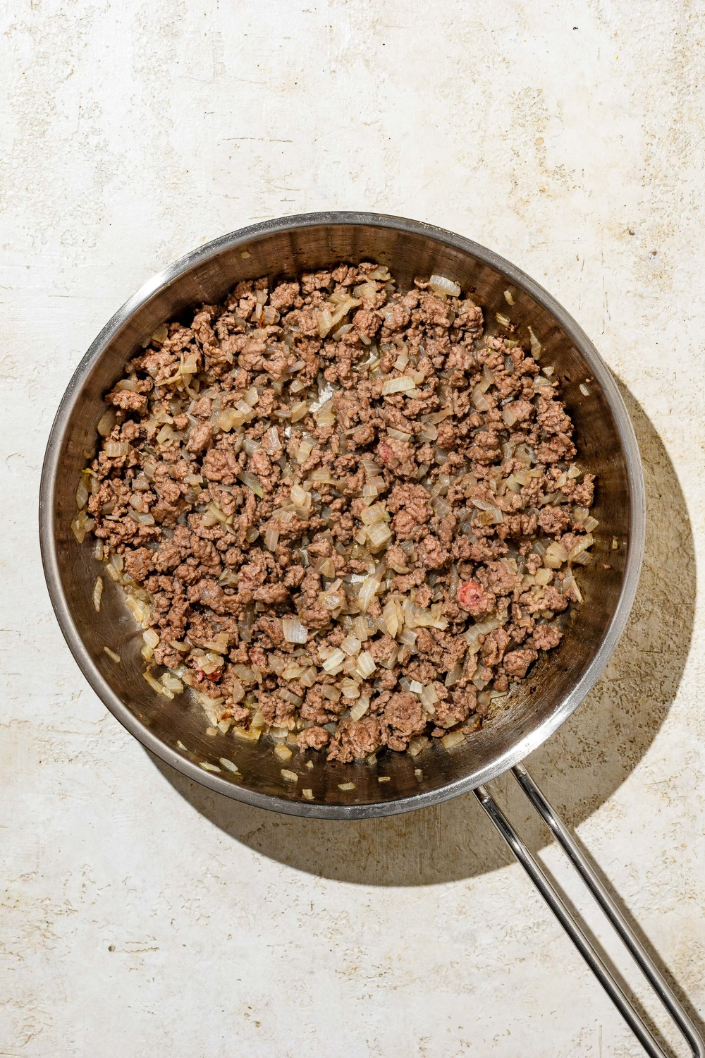 A skillet with browned beef cooked with onion. The skillet is on a tan counter.
