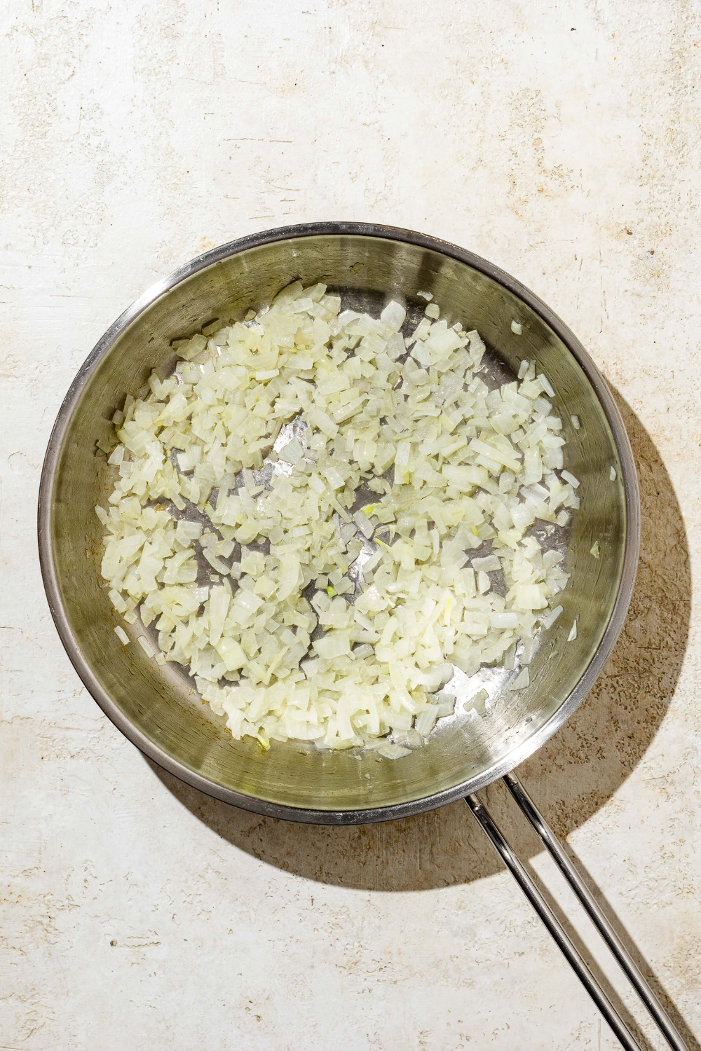 A skillet with chopped onion cooking in oil. The skillet is on a tan counter.