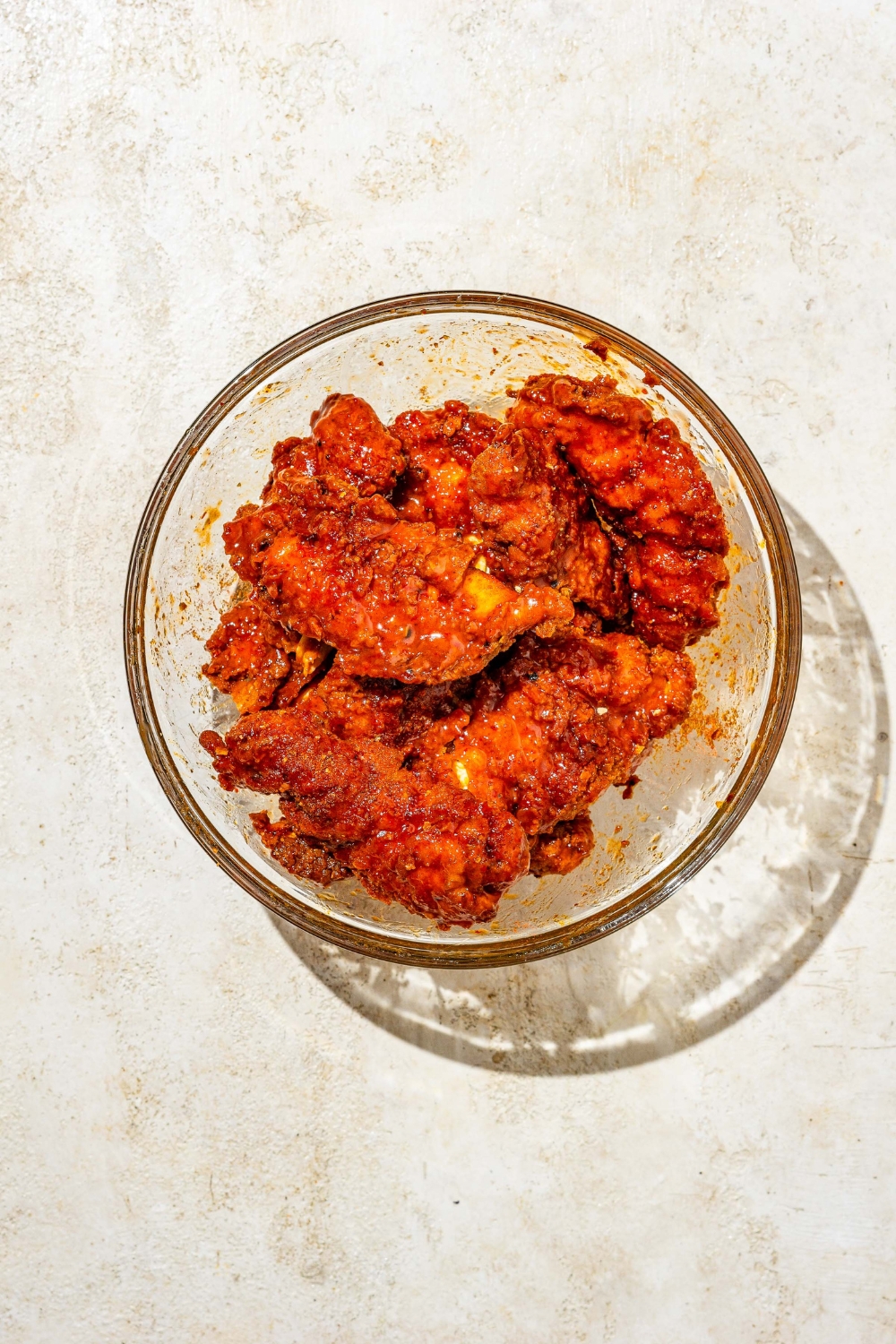 A glass bowl with fried chicken tenders tossed in honey honey sauce and seasonings. The bowl is on a tan counter.