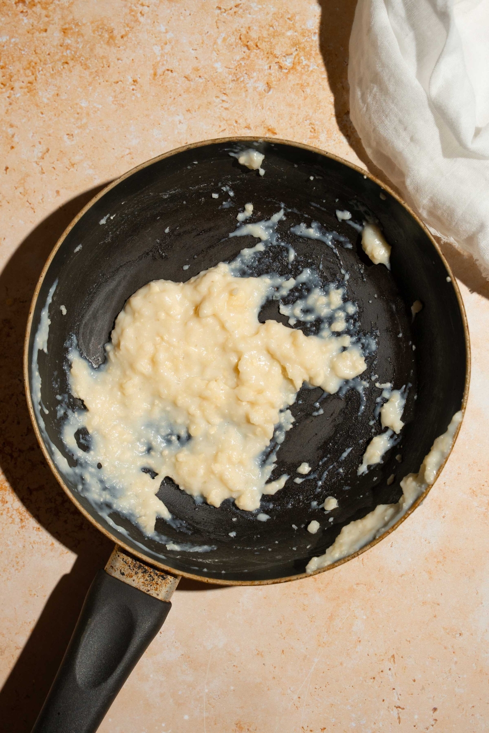 A skillet with a water, milk, and flour mixture. The skillet is on a tan counter.