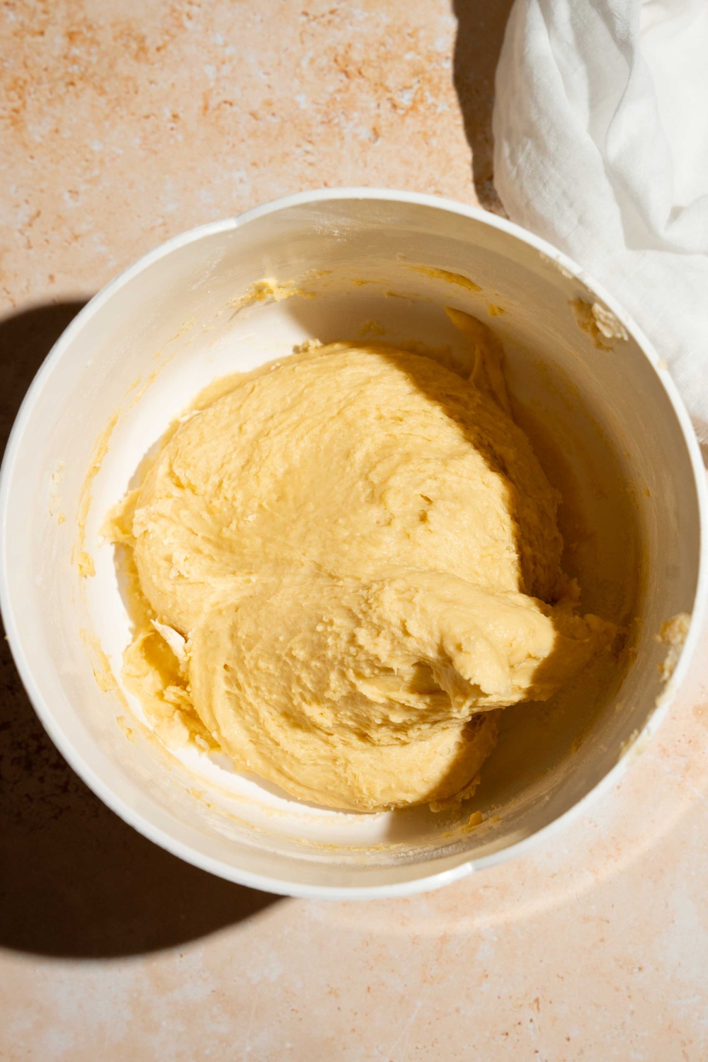 A large mixing bowl with a dough mixture. The bowl is on a tan counter.