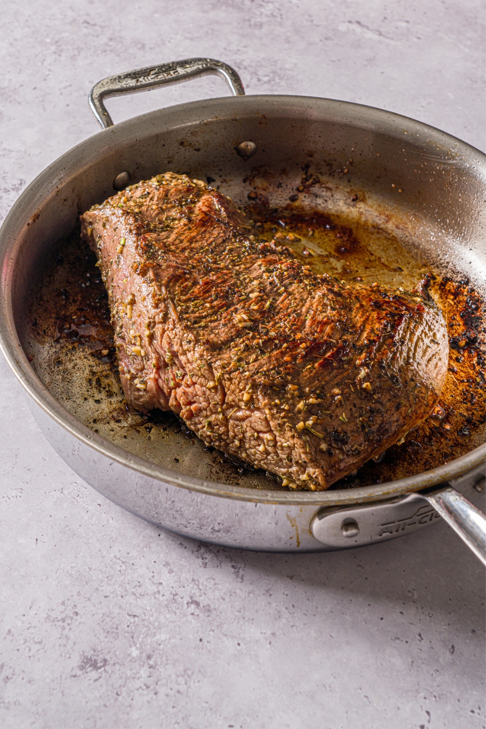 A skillet with marinated steak searing in oil. The skillet is on a stone counter.