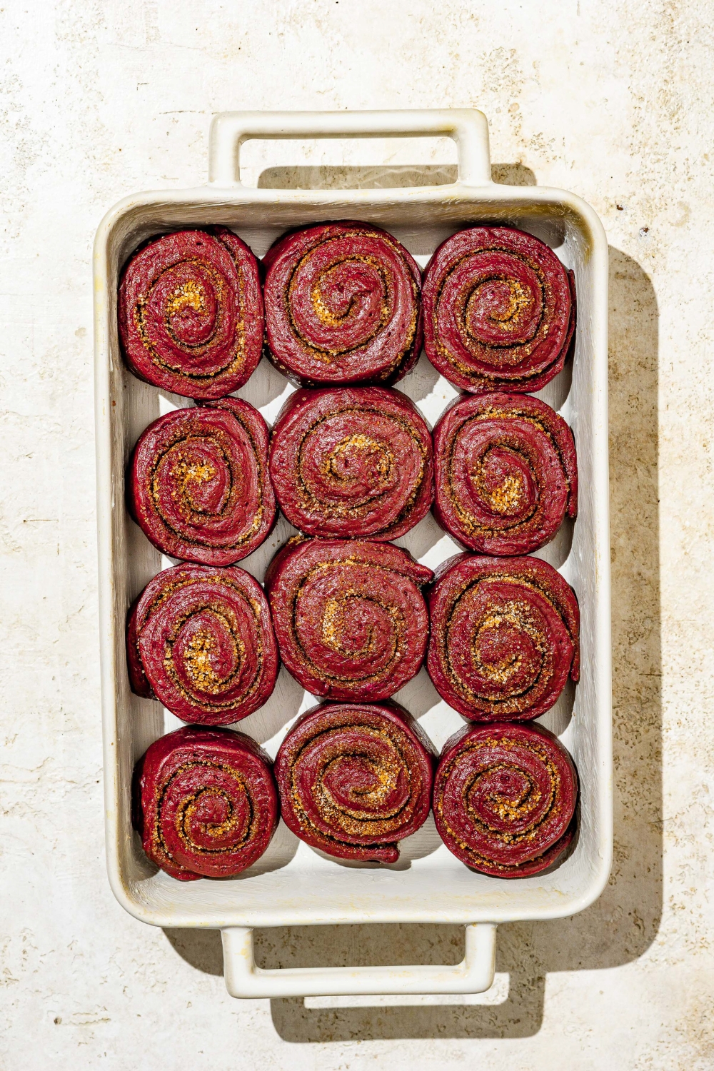 A baking dish with uncooked red velvet cinnamon rolls. The dish is on a tan counter.