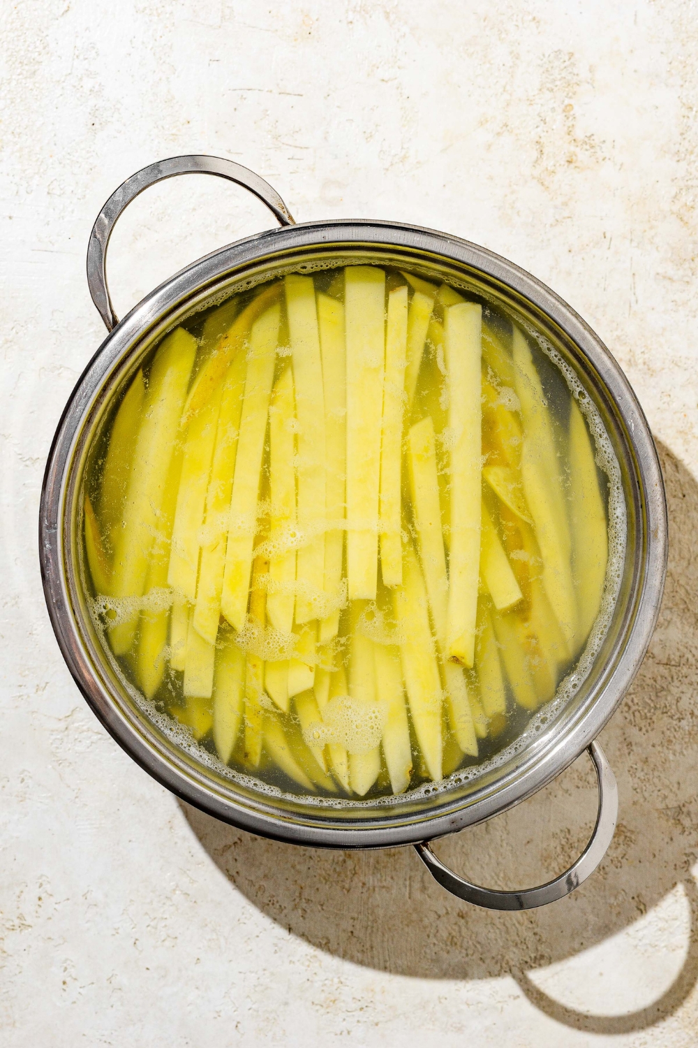 A stock pot with sliced fries soaking in water. The pot is on a white counter.