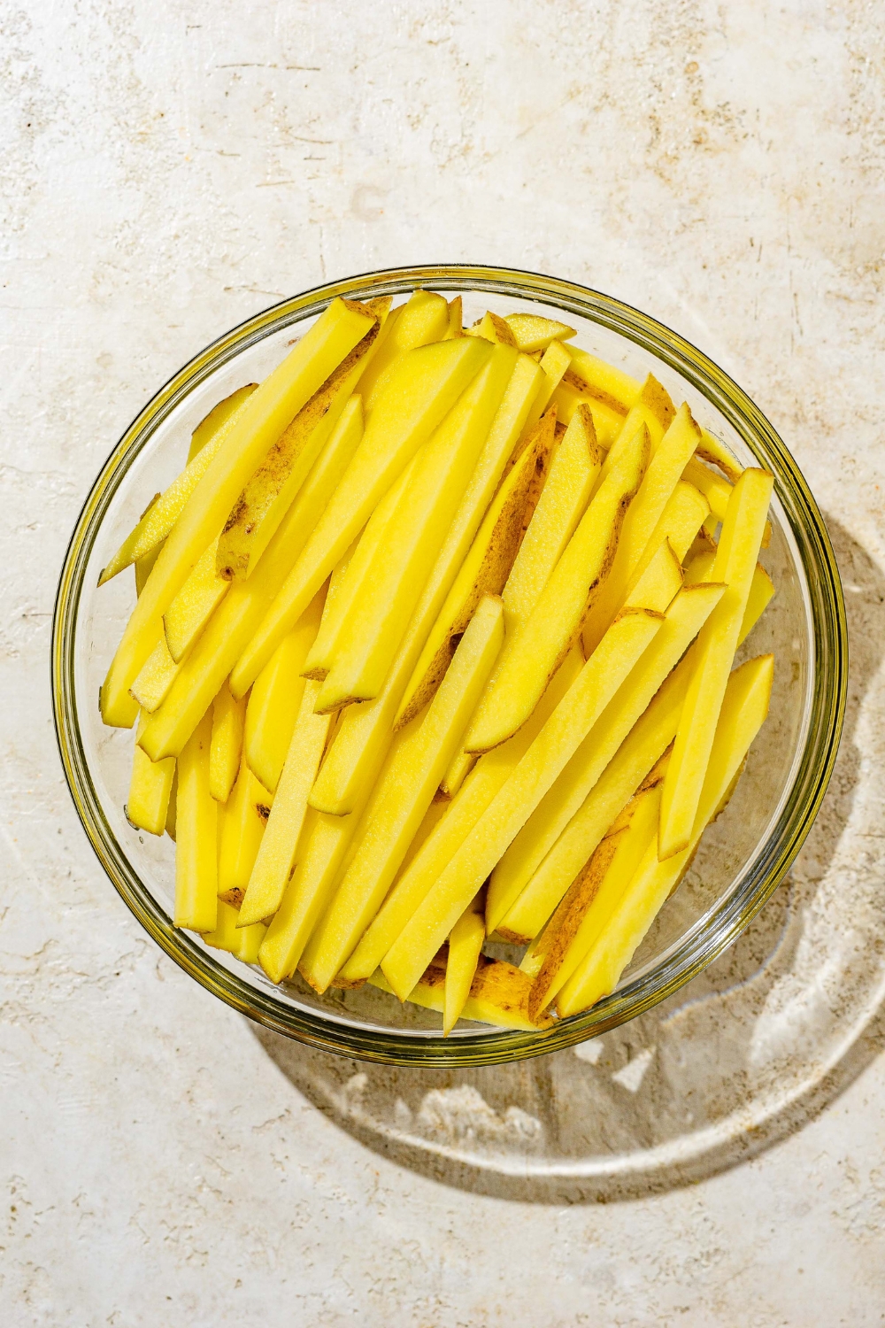 A glass bowl with sliced french fries. The bowl is on a white counter.