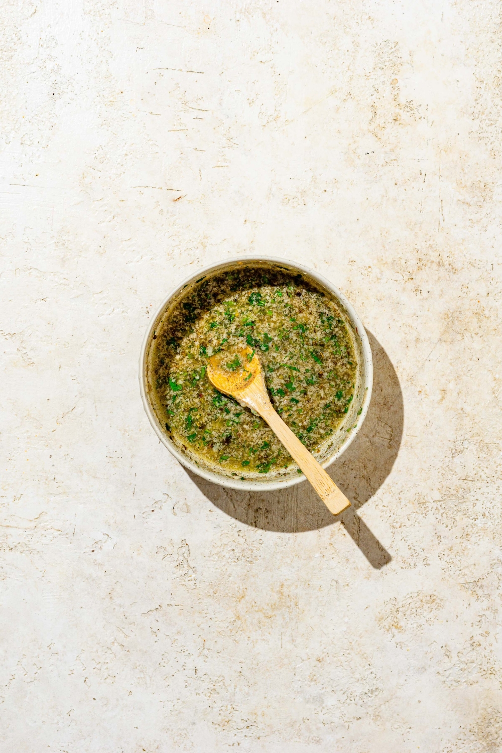 A white bowl with mixed garlic parmesan butter with a wooden spoon in the bowl.