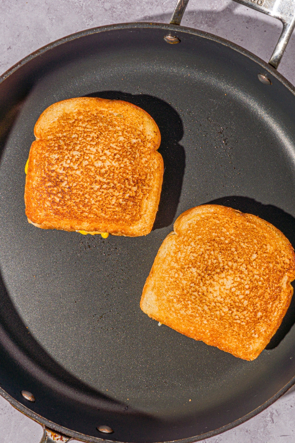 A skillet with two grilled cheeseburgers. The skillet is on a stone counter.