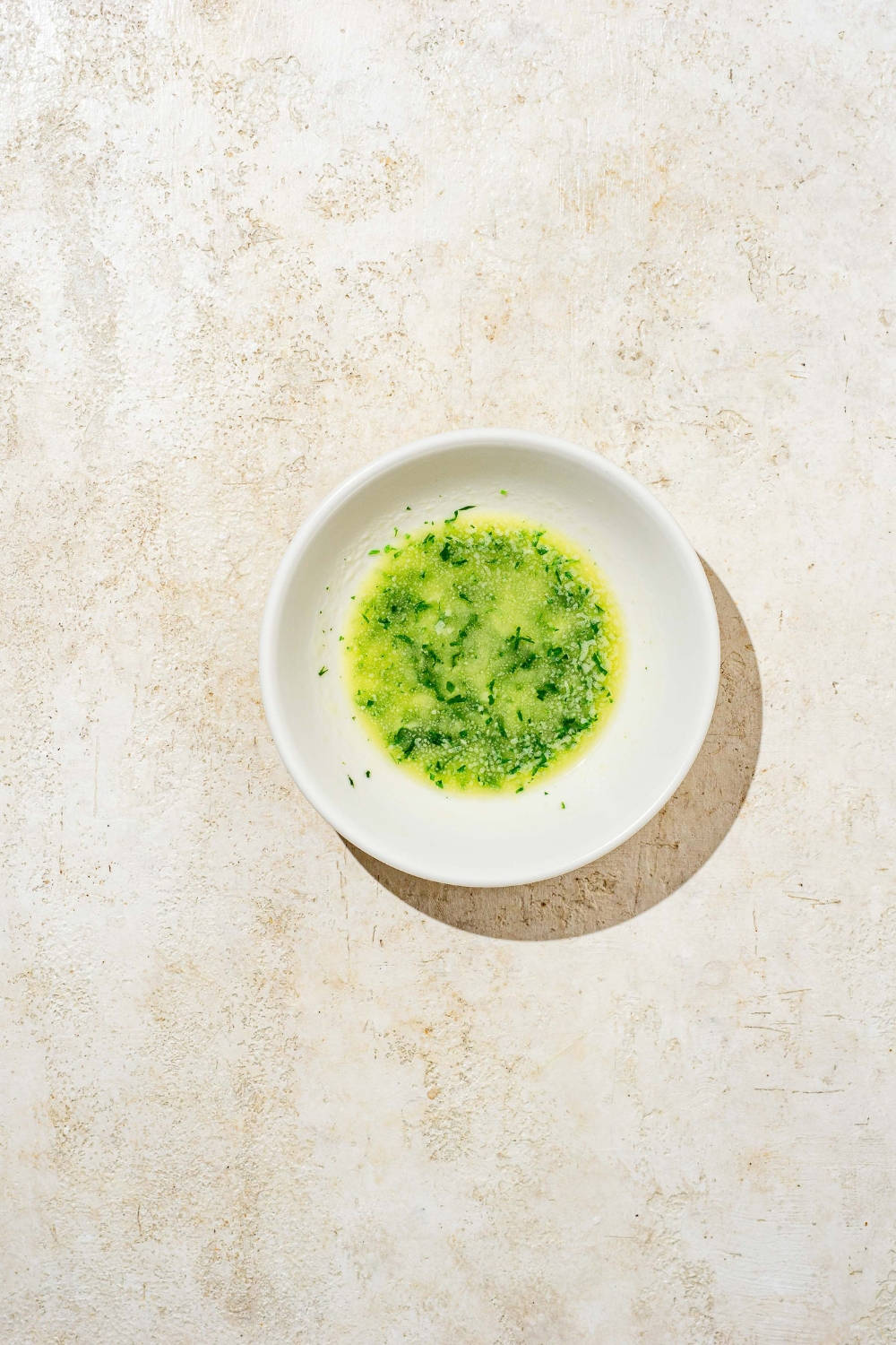A glass bowl with melted butter and parsley. The bowl is on a tan counter.