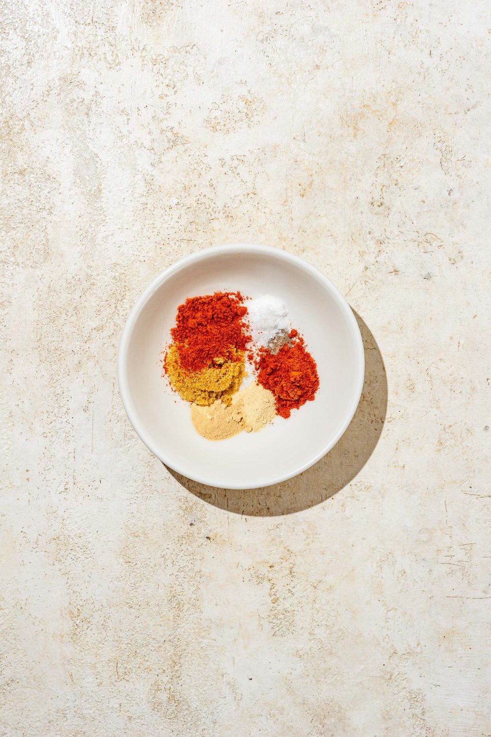 A small bowl of seasonings to make a hot honey chicken dry rub. The bowl is on a tan counter.