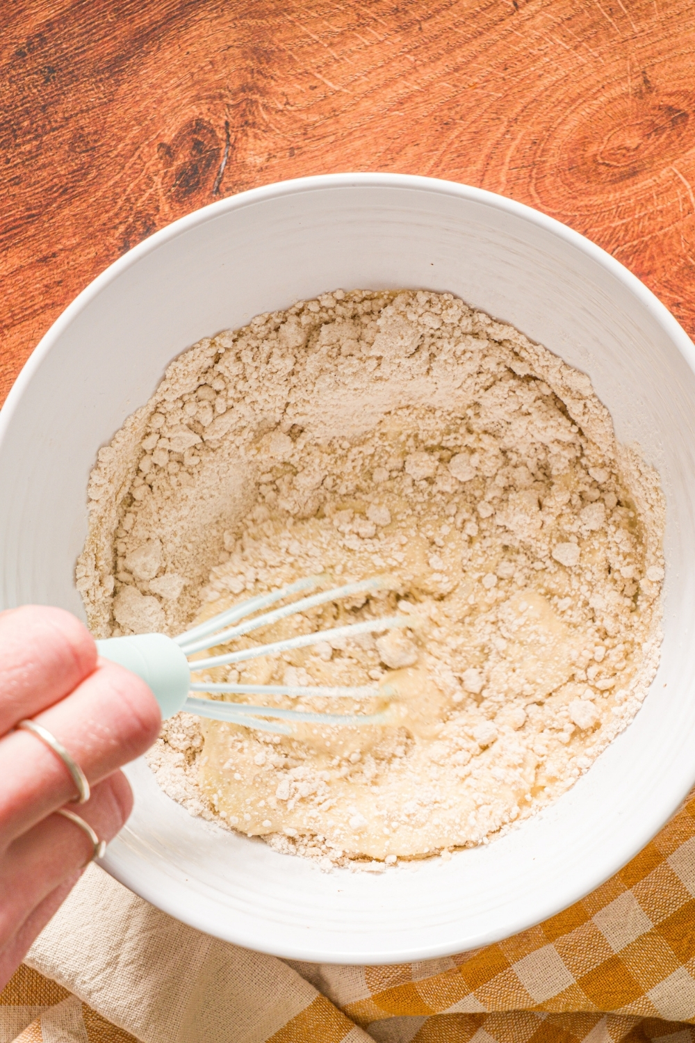 A white bowl with a whisk mixing dry ingredients to make muffin mix pancakes. The bowl is on a wooden counter.