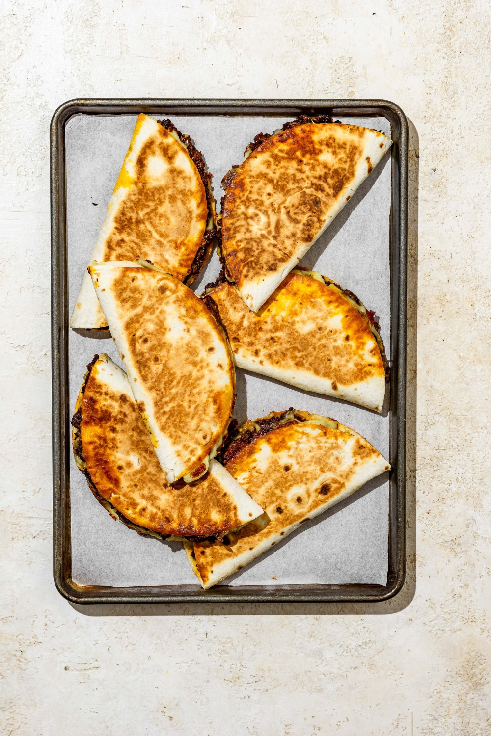 A baking sheet lined with parchment paper with several crispy beef tacos. The baking sheet is on a tan counter.
