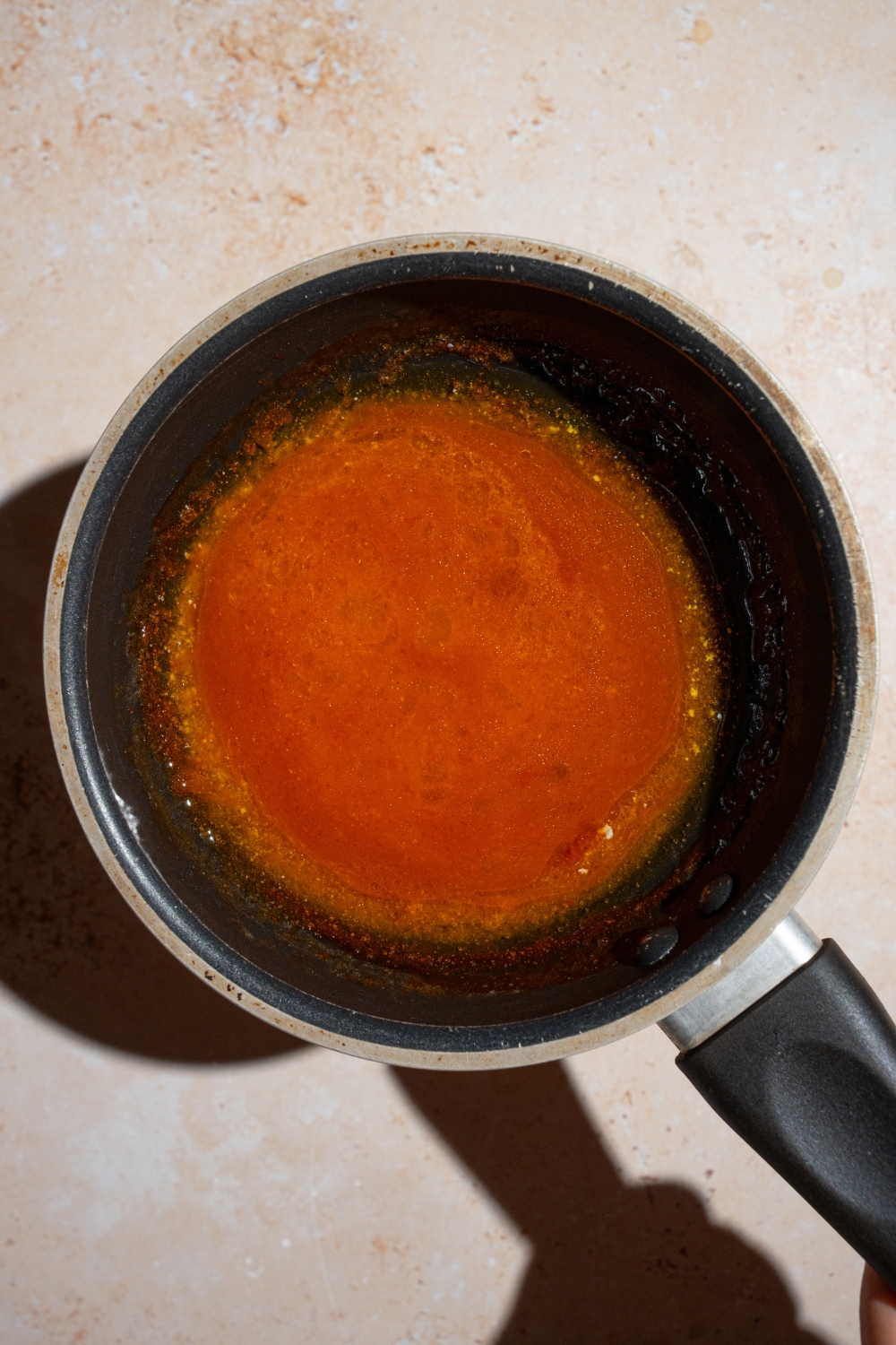 A skillet with cooked Buffalo sauce. The skillet is on a tan counter.