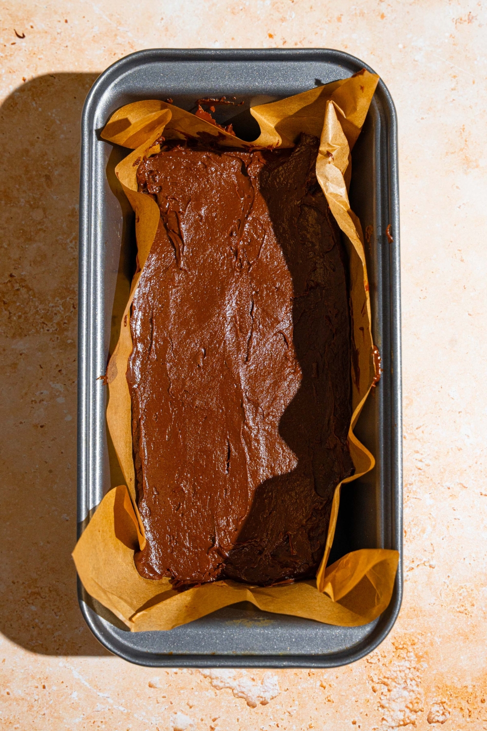 A bread pan lined with parchment paper filled with a fudge mixture. The pan is on a tan counter.