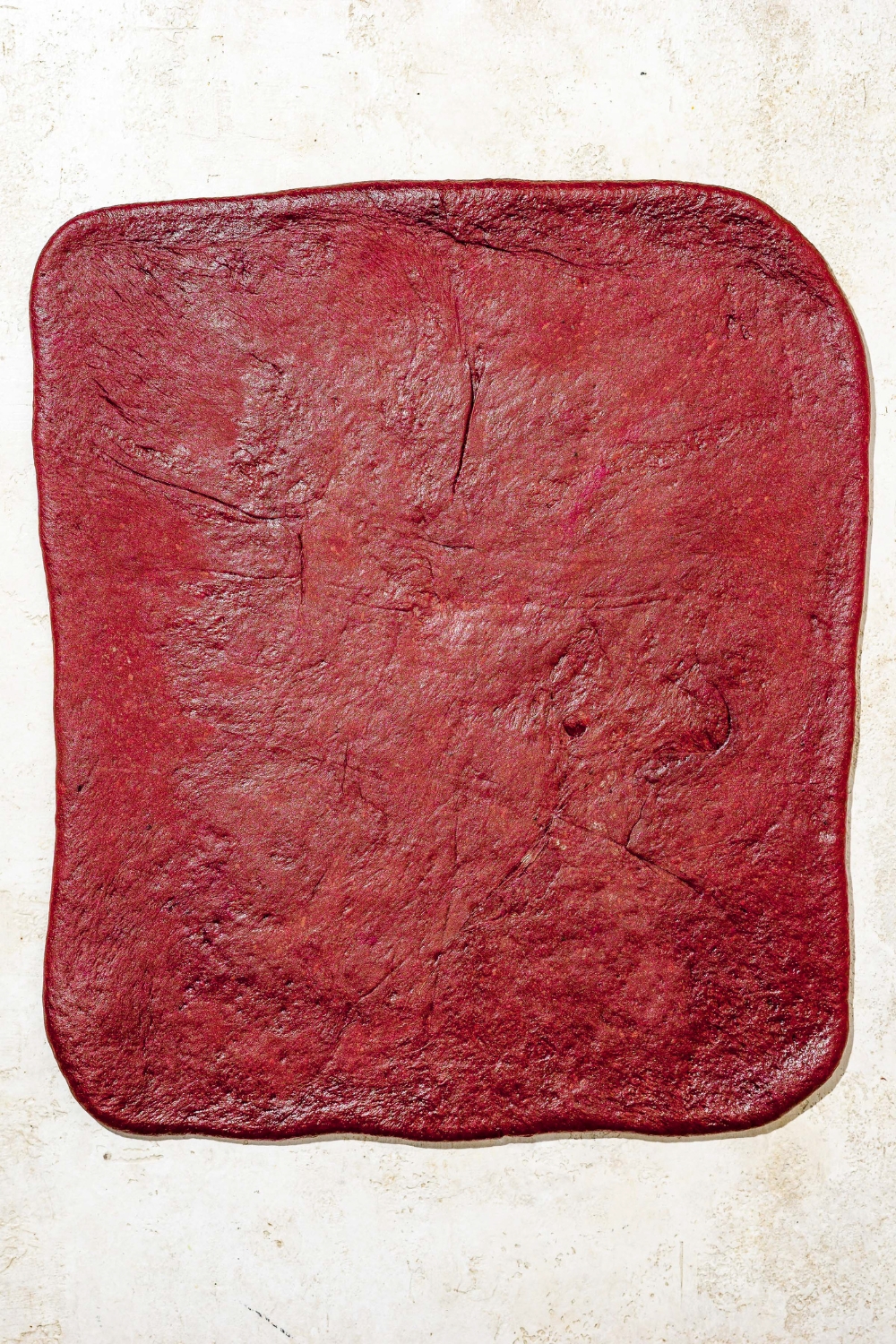 Red velvet cinnamon roll dough rolled out into a rectangle. The dough is on a tan counter.