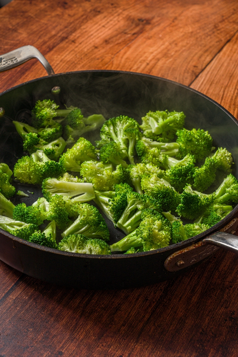 A skillet with steamed broccoli. The skillet is on a wooden counter.