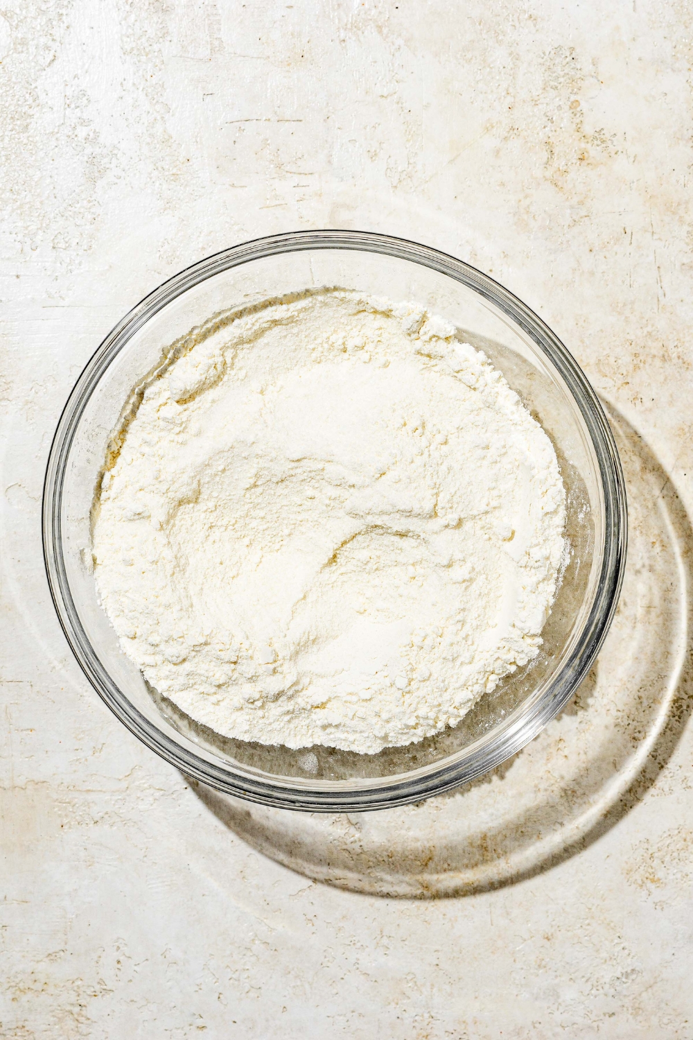 A glass bowl with dry ingredients to make white Texas sheet cake batter including flour, baking powder, salt, and sugar. The bowl is on a white counter.