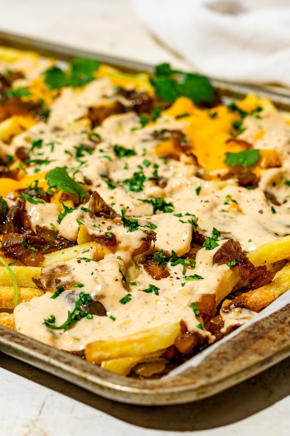 A baking sheet of In n Out animal style fries topped with melted American cheese, caramelized onions, animal sauce, and fresh parsley. The sheet is on a tan counter.