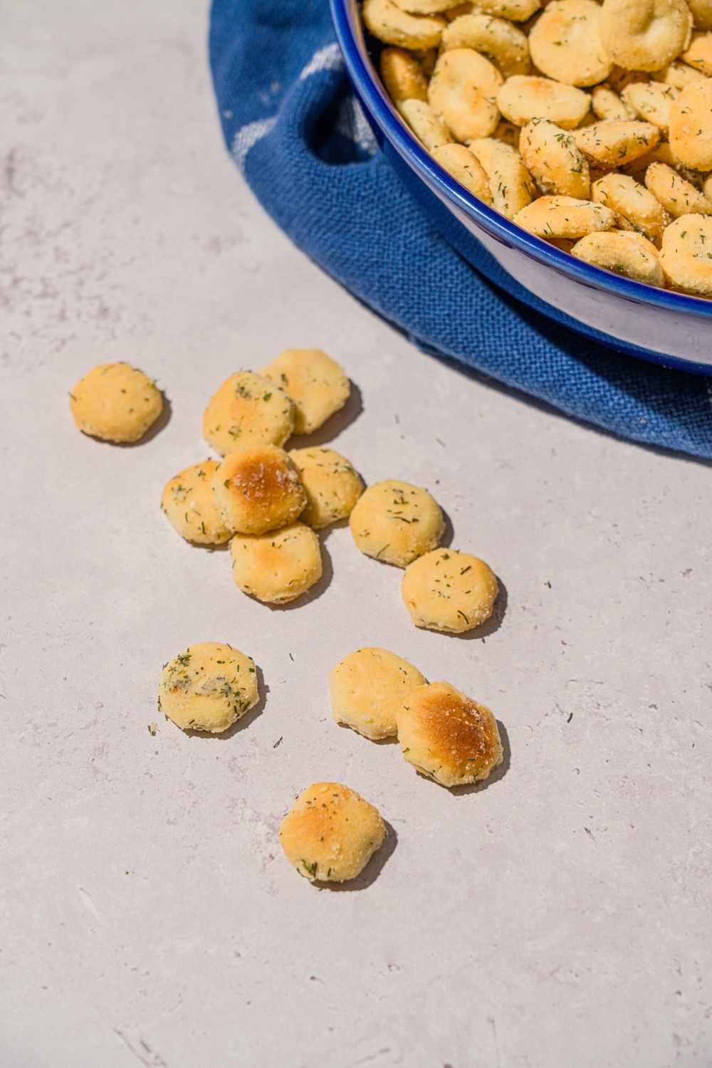 Several ranch oyster crackers on a white counter next to a bowl of crackers with a blue striped napkin.