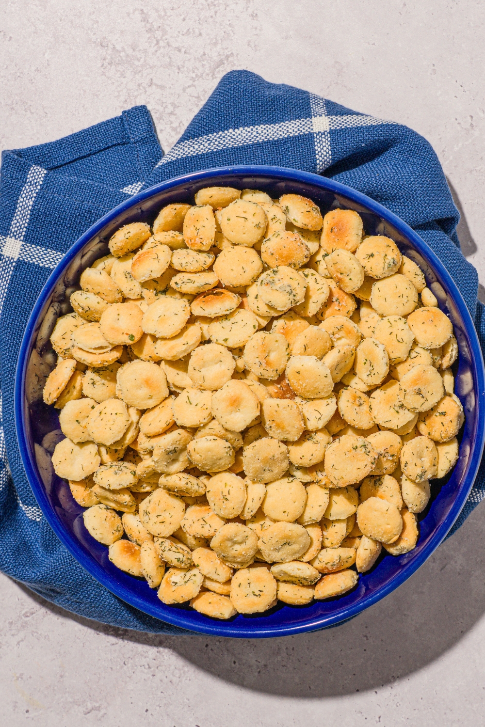 A blue bowl filled with ranch oyster crackers. The bowl is on a white counter with a blue striped napkin.