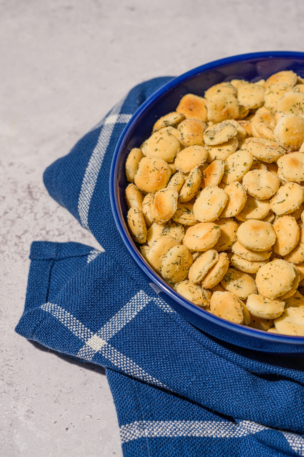 A blue bowl filled with ranch oyster crackers. The bowl is on a white counter with a blue striped napkin.