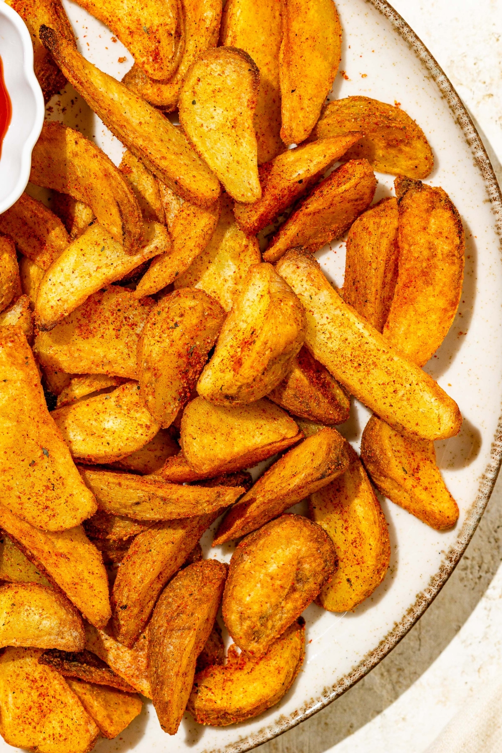 A white plate with wedge fries seasoned with Red Robin seasoning. The plate is on a tan counter.