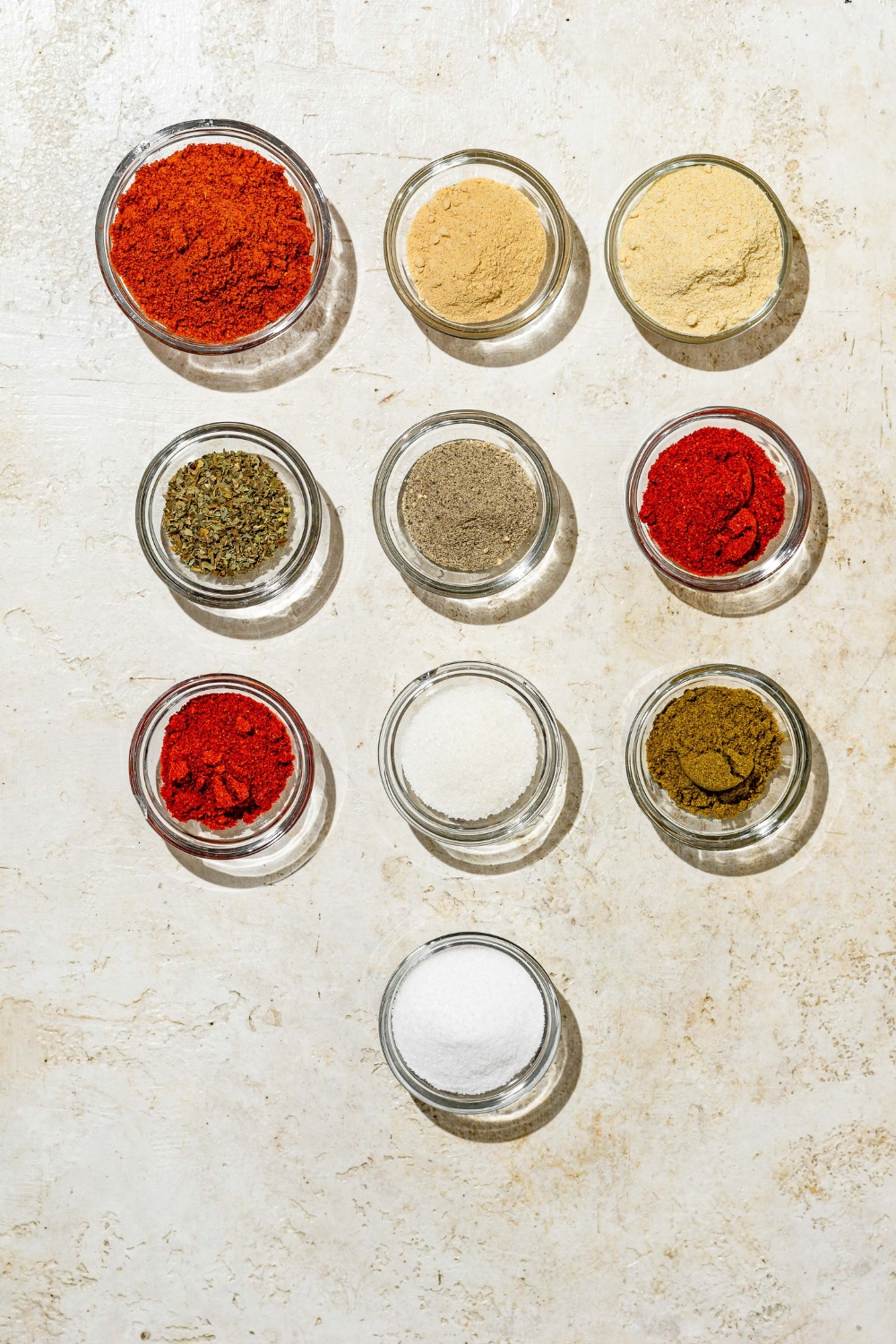 An overhead shot of several bowls containing ingredients to make Red Robin seasoning including paprika, cumin, garlic powder, onion powder, salt, celery salt, dried basil, chili powder, salt, and pepper.