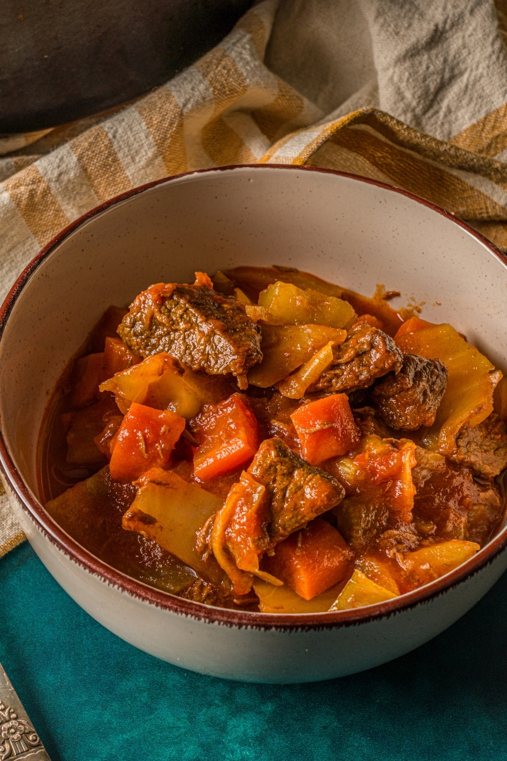 A bowl of beef cabbage stew on a blue counter with a yellow striped napkin.
