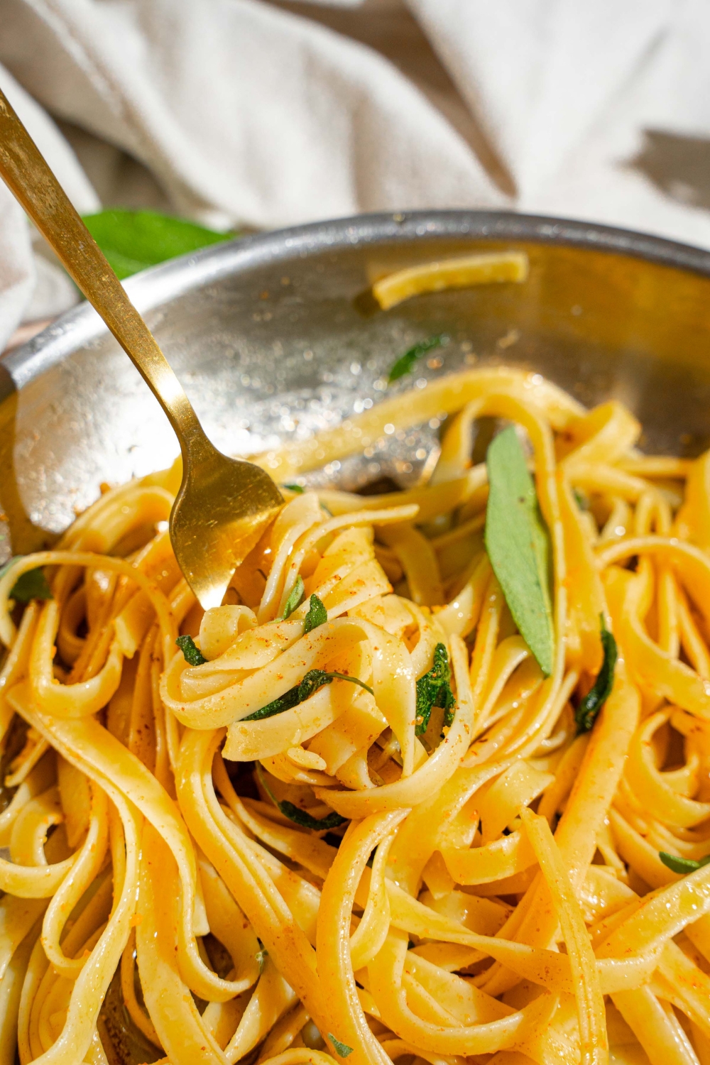 A skillet with a fork twirling a bite of linguine pasta in brown butter sauce with sage.