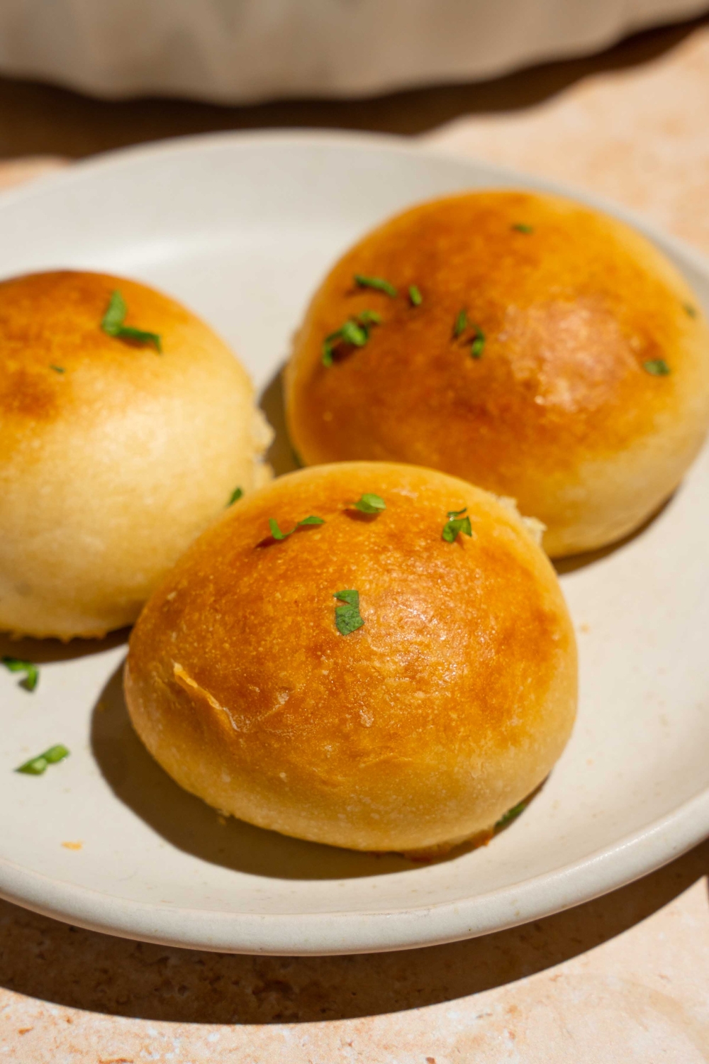 A white plate with three dinner rolls brushed with garlic herb butter and garnished with parsley.