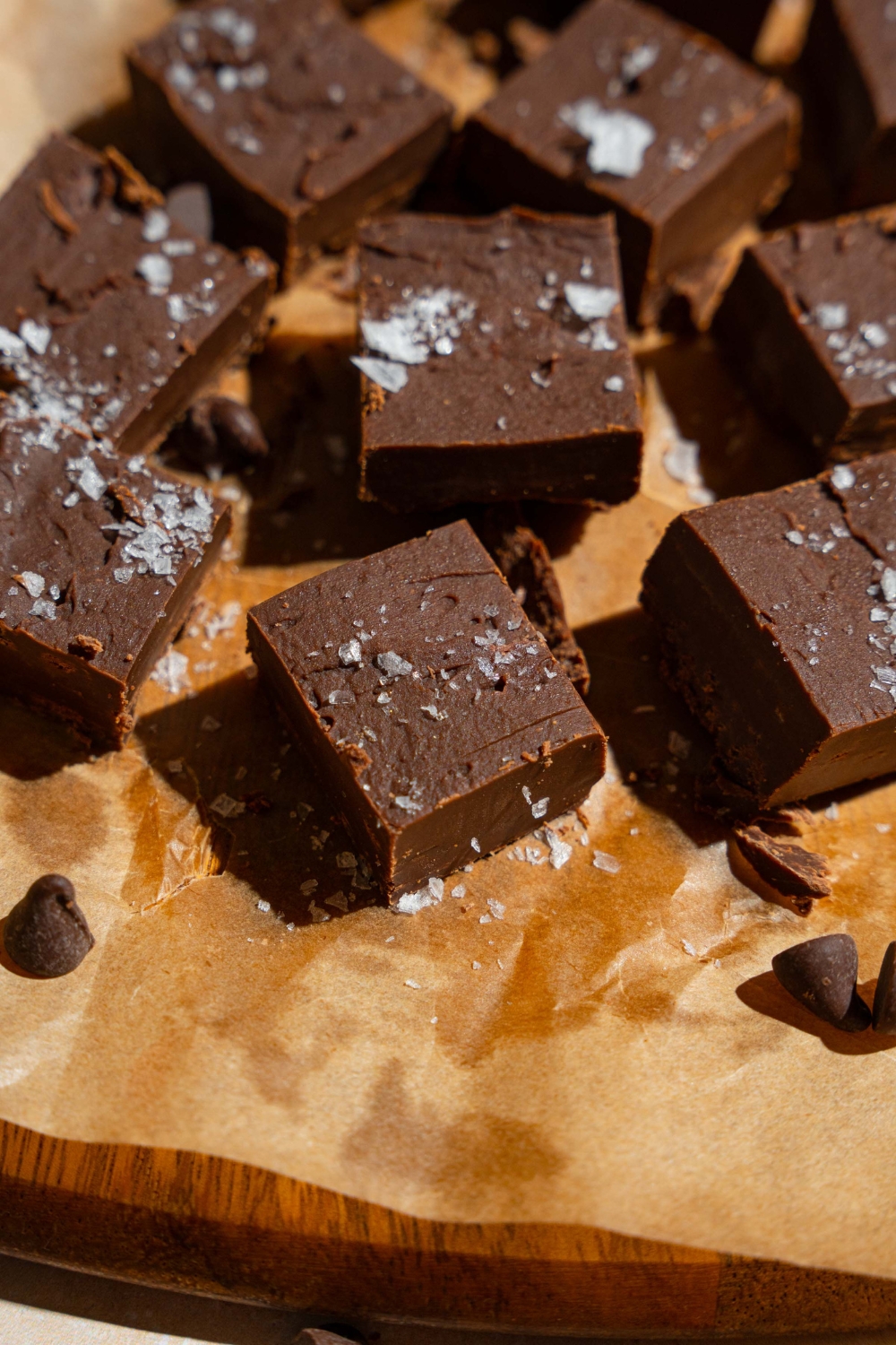 Sliced fudged pieces topped with flaky sea salt on a wooden board lined with parchment paper.