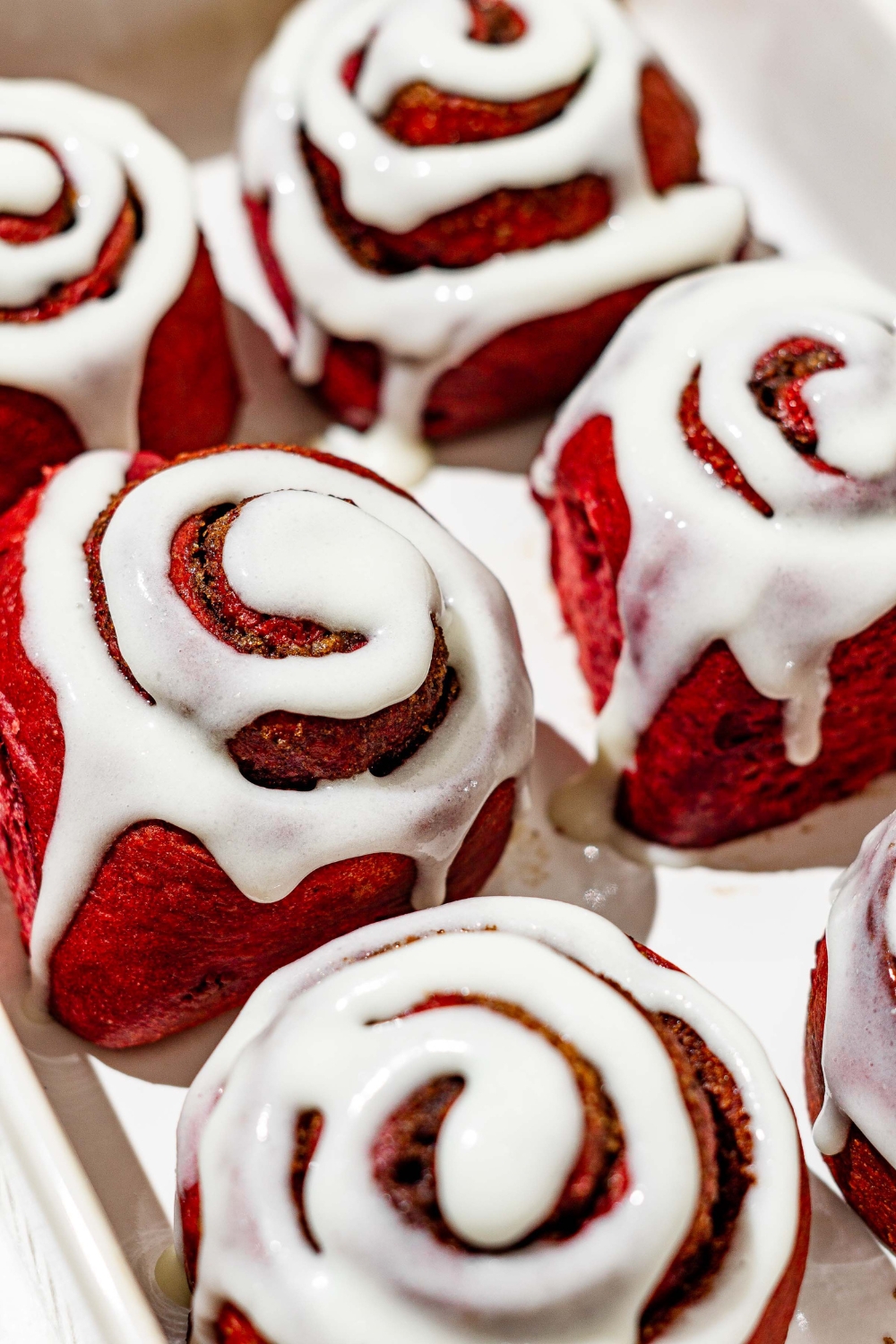 Six red velvet cinnamon rolls with cream cheese frosting in a baking dish.