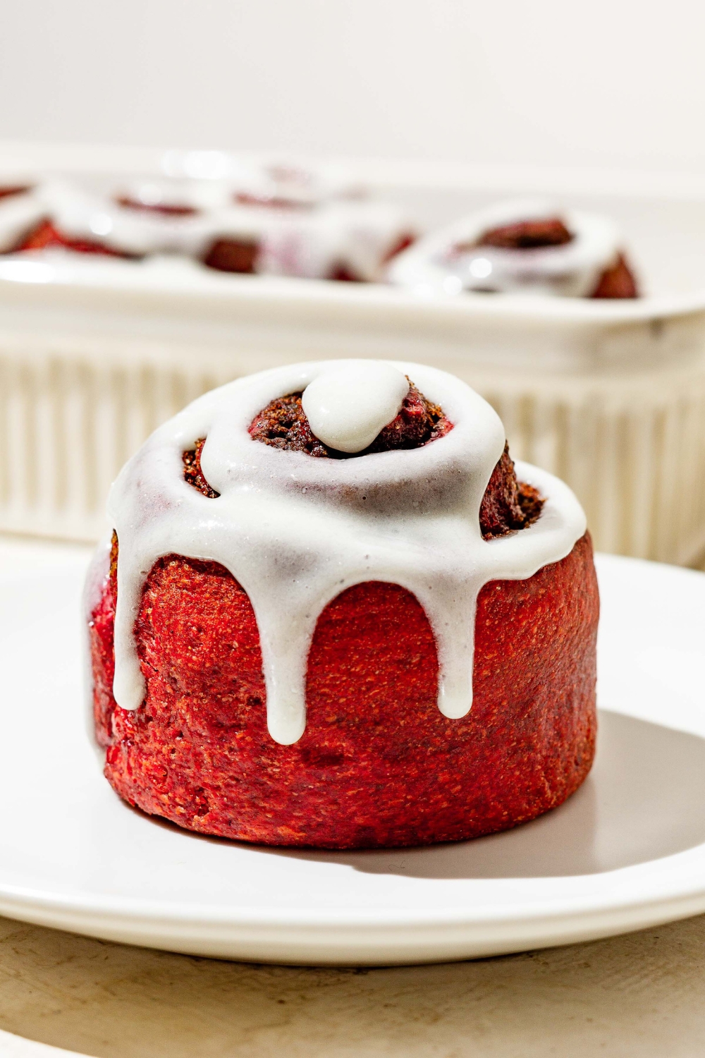 A red velvet cinnamon roll with cream cheese frosting on a white plate.