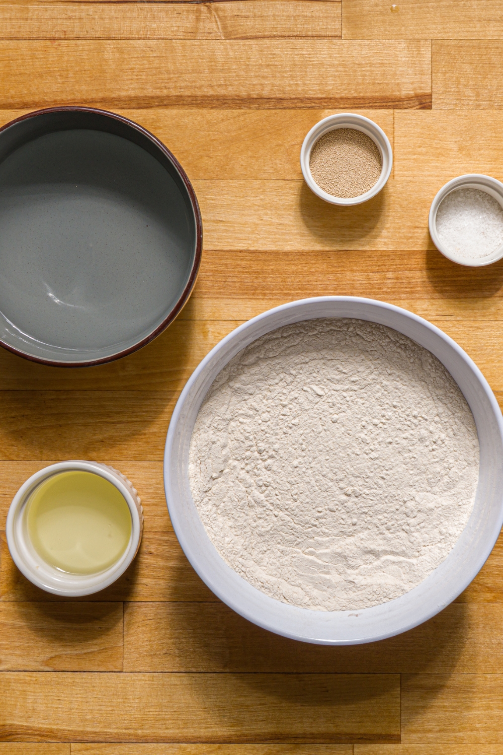 Several bowls in various sizes containing ingredients to make Auntie Anne's pretzels including flour, yeast, salt, brown sugar, water, and oil.