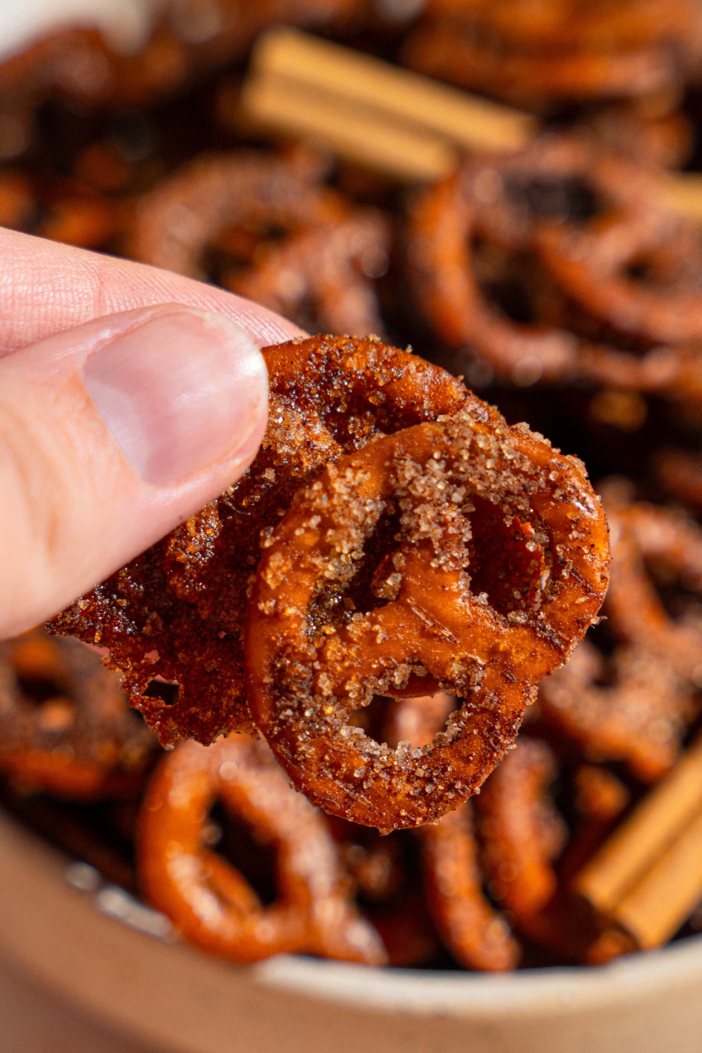 A close up of a hand holding a cinnamon sugar pretzels with a bowl of pretzels blurred in the background.