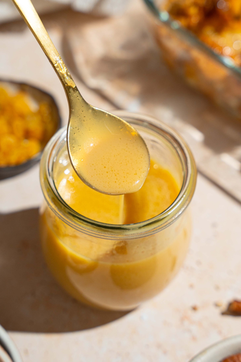 A glass jar with rum sauce for bread pudding. A spoon is dipped in the jar. The jar is on a tan counter.