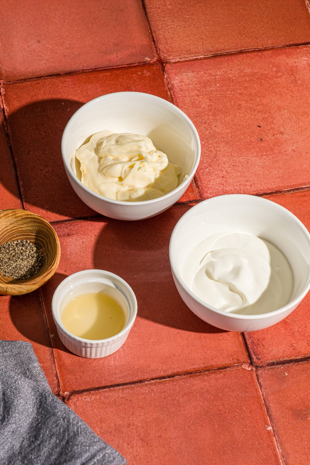 Several bowls in various sizes containing ingredients to make shishito pepper dipping sauce including mayo, sour cream, lime juice, and pepper.