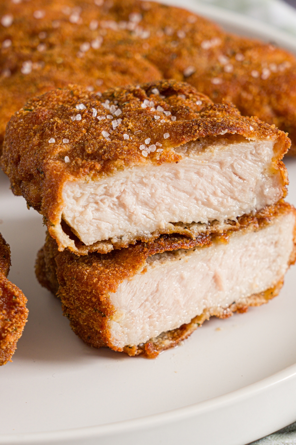 A white plate with crispy breaded pork cutlets seasoned with salt. One cutlet is sliced in half and stacked on top of each other.