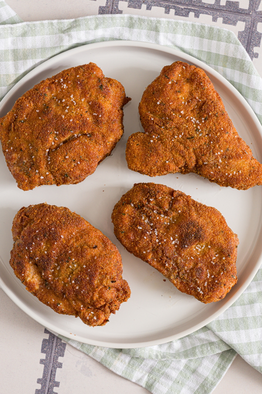 A white plate with crispy breaded pork cutlets seasoned with salt. The plate is on a tiled counter with a green cloth napkin.