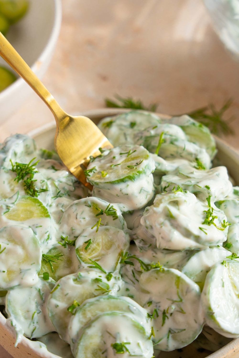 A bowl of cucumber dill salad tossed with a yogurt and sour cream dressing with fresh dill. There is a fork in the bowl.