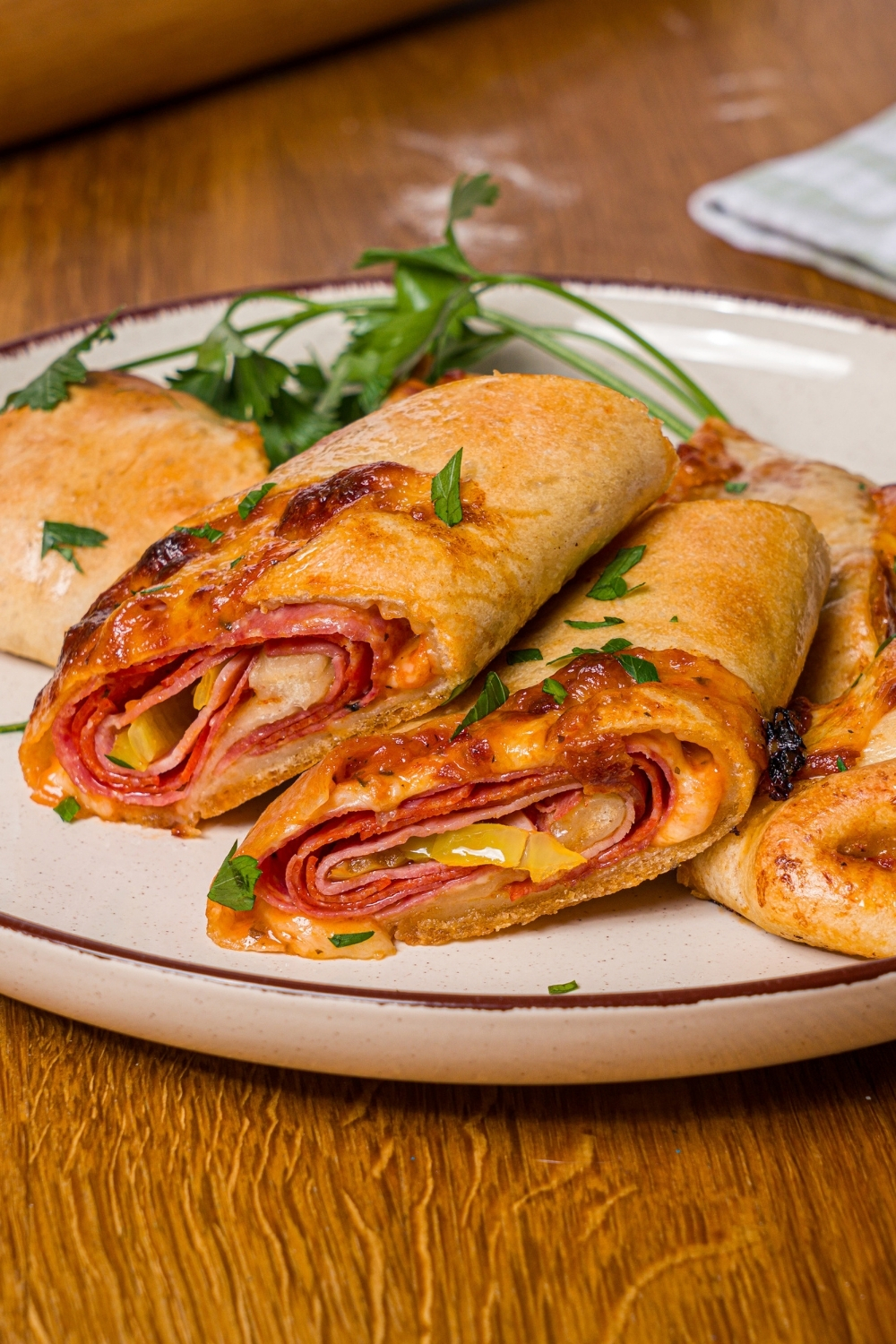 A white plate with sliced stromboli garnished with fresh parsley. The plate is on a wood counter.