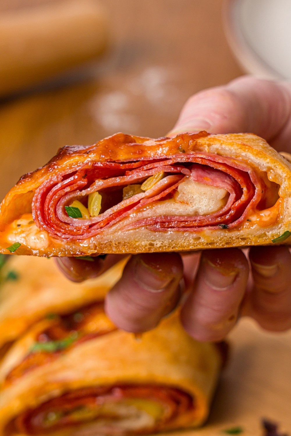 A close up of a hand holding a slice of stromboli. There is a plate of sliced stromboli blurred in the background.